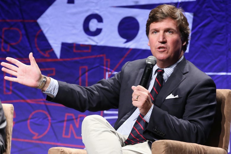 Tucker Carlson speaks into a microphone as he sits on a stage.